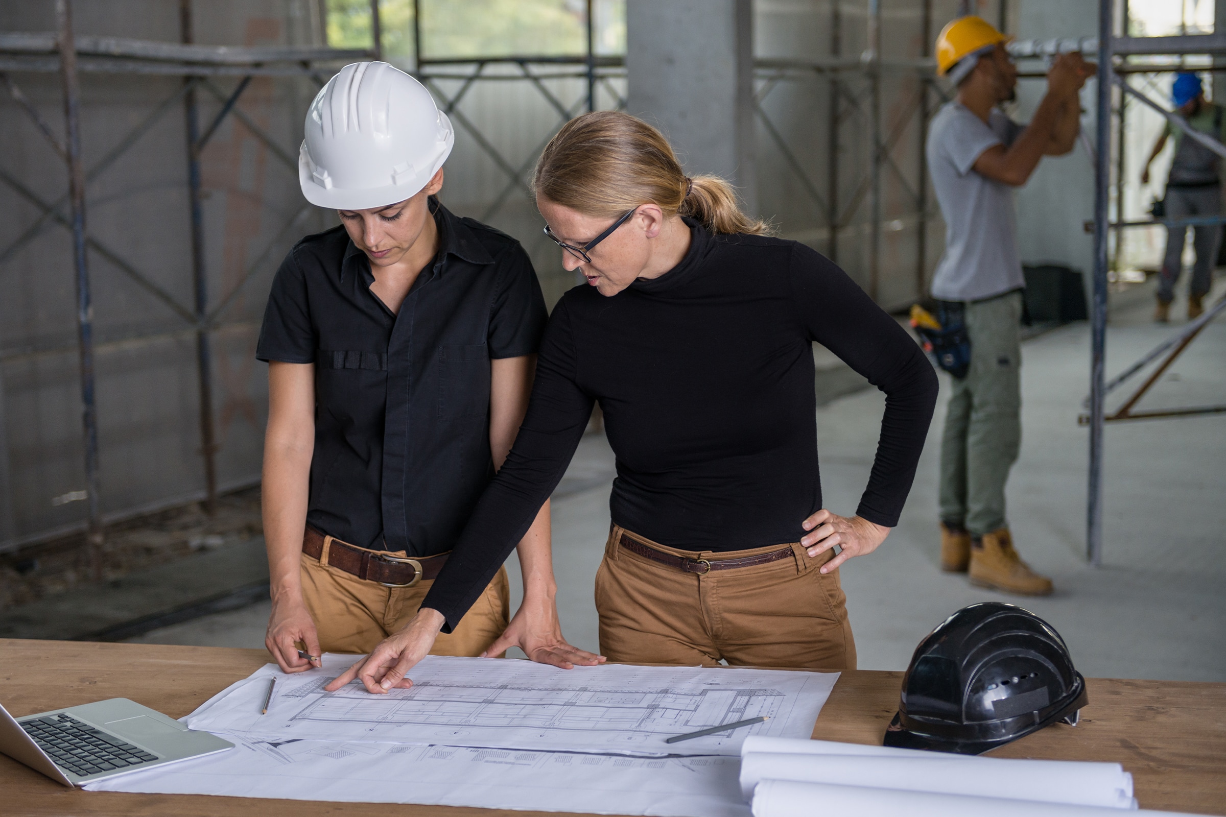 two women discussing plans with construction workers behind them
